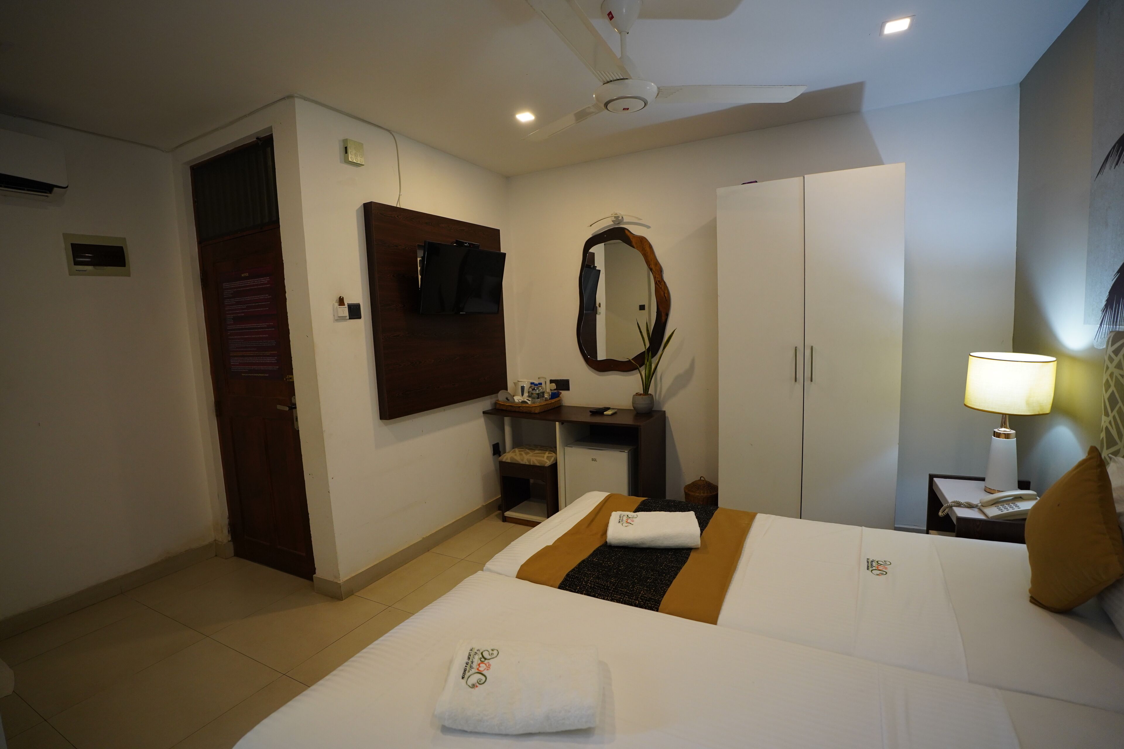 Ein Hotelzimmer mit Bett, Schreibtisch, Spiegel, Kleiderschrank, Nachttisch mit Lampe und Deckenventilator.