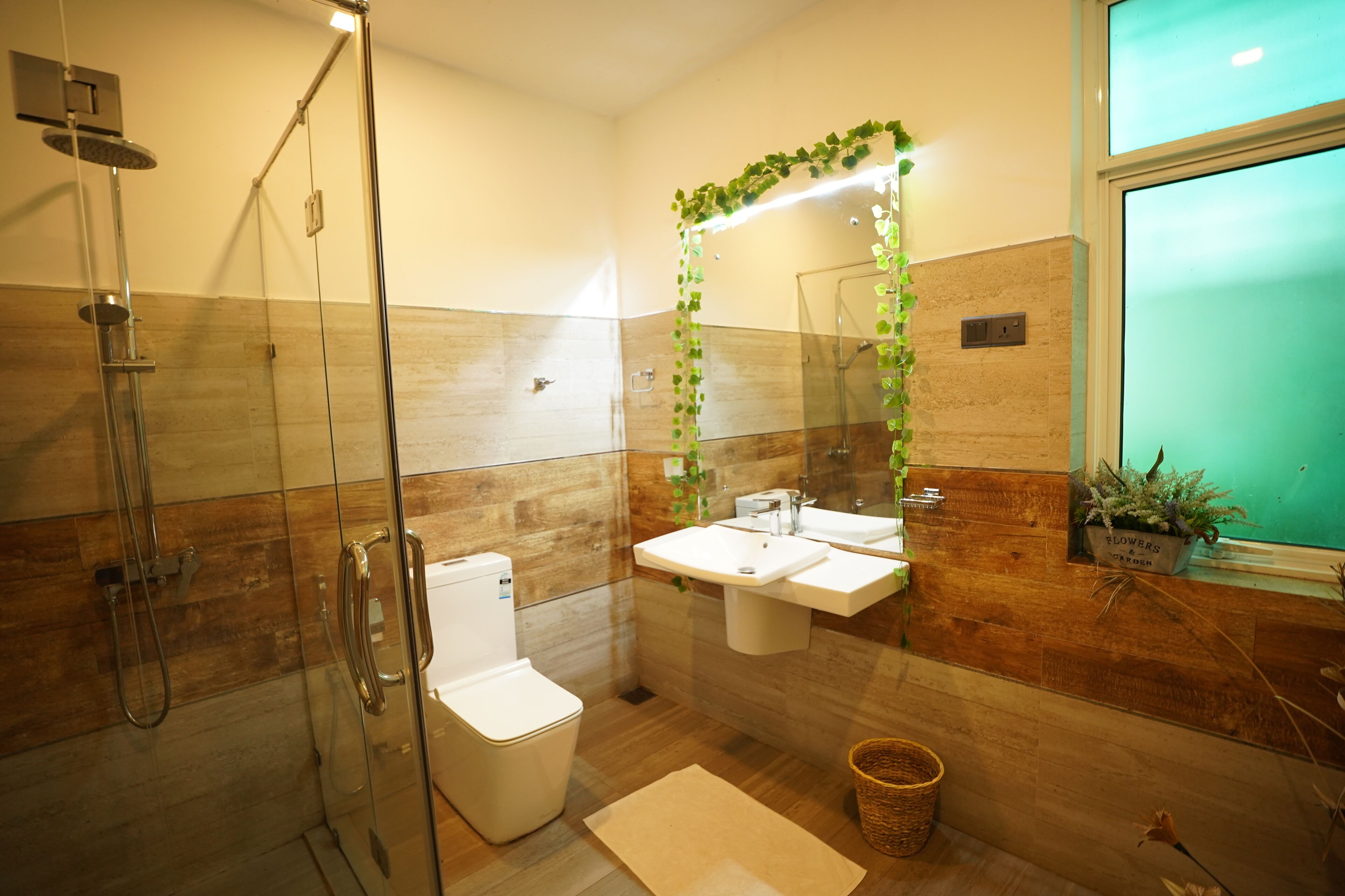 Un baño moderno con cabina de ducha de vidrio, inodoro, lavabo y espejo con un arco de hojas verdes.