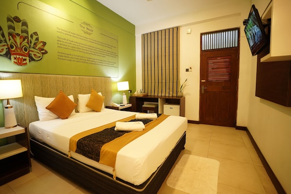 Hotelkamer met een groot bed, een bureau, een televisie en een groene muur met een verzameling maskers.