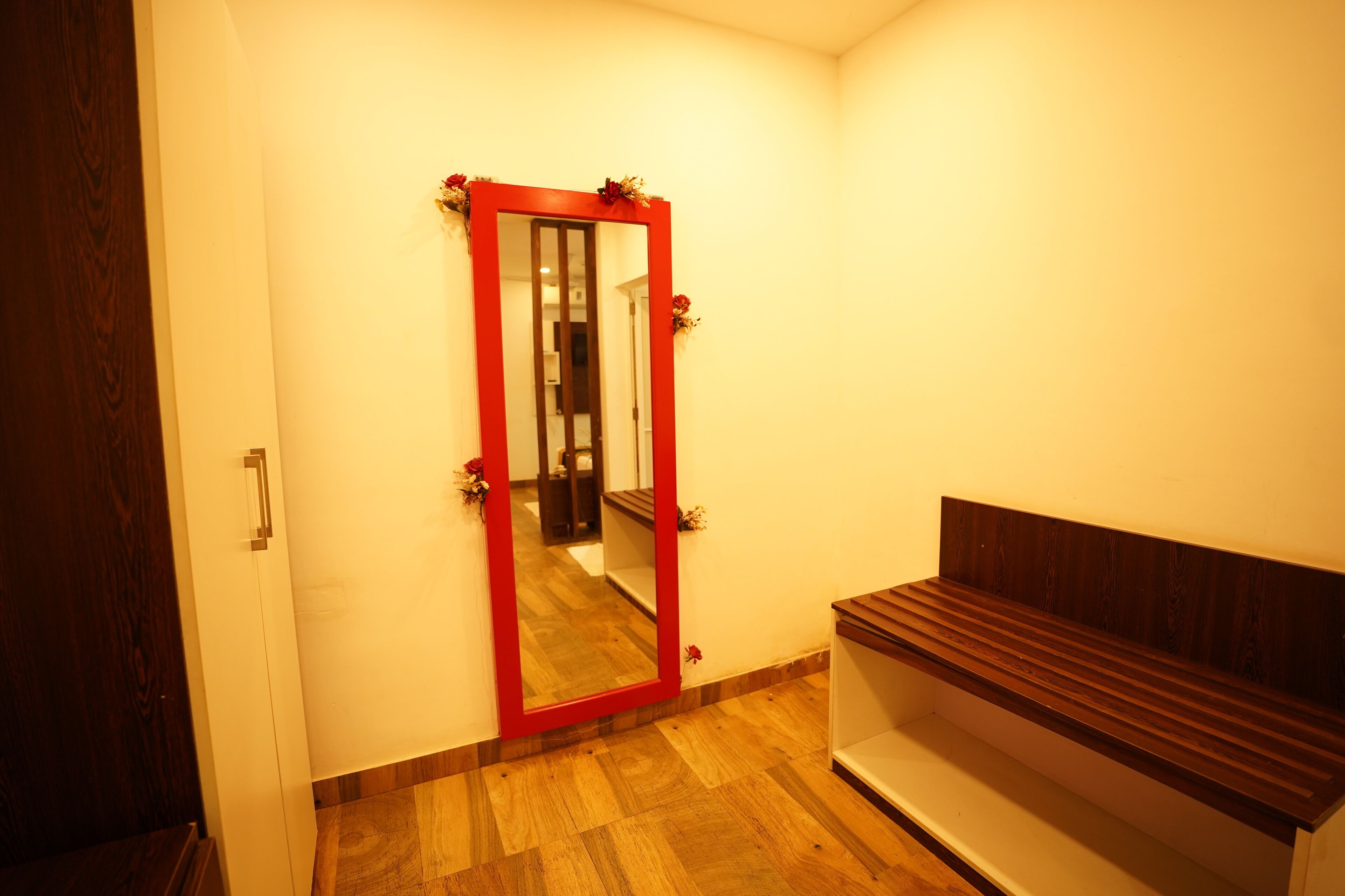 Una habitación con un banco de madera, un espejo de marco rojo y una puerta de madera.