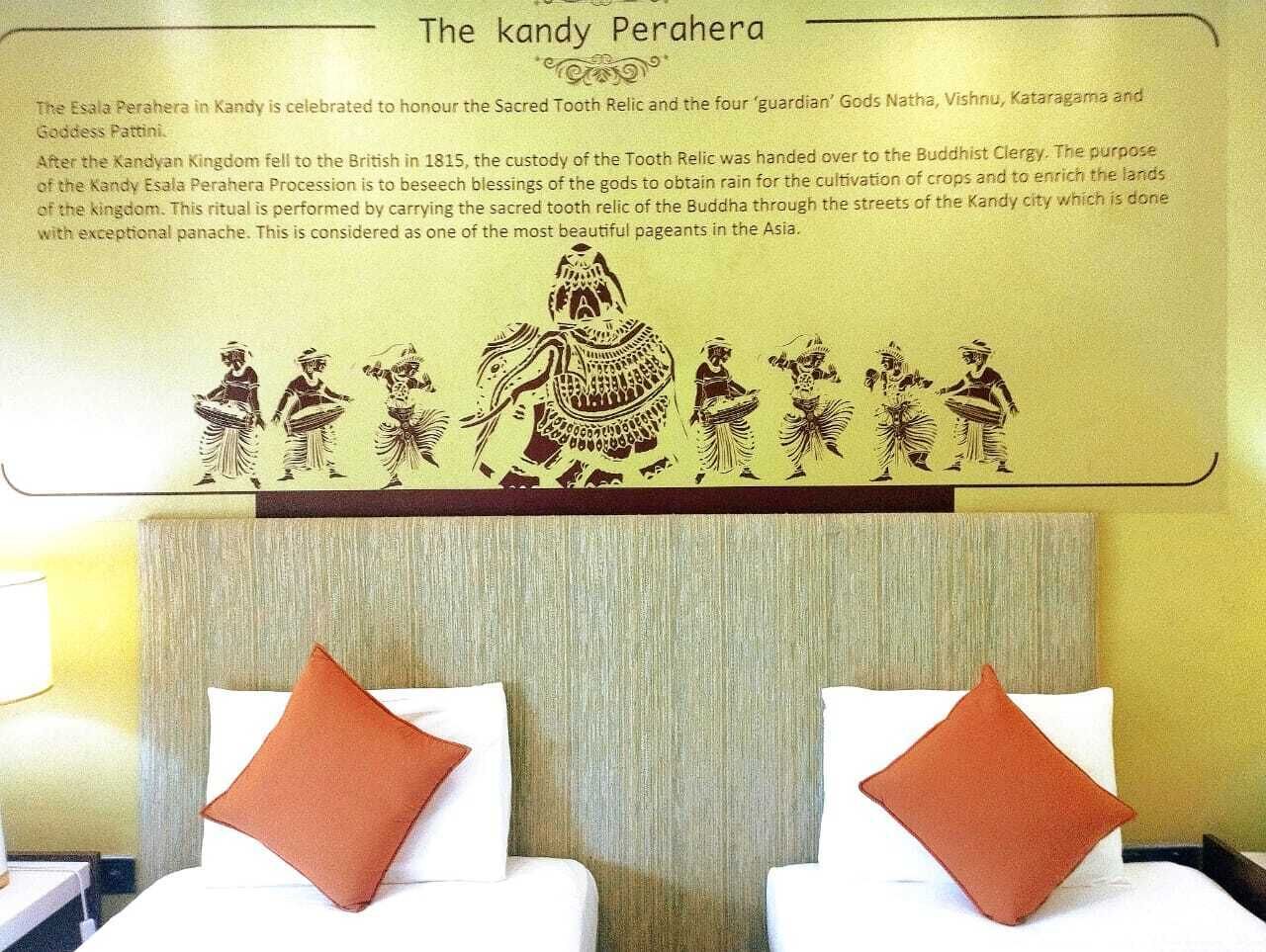 A hotel room with a bed, two pillows, a headboard, and a wall with a cultural mural.