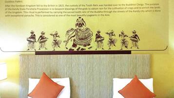 A hotel room with a bed, two pillows, a headboard, and a wall with a cultural mural.