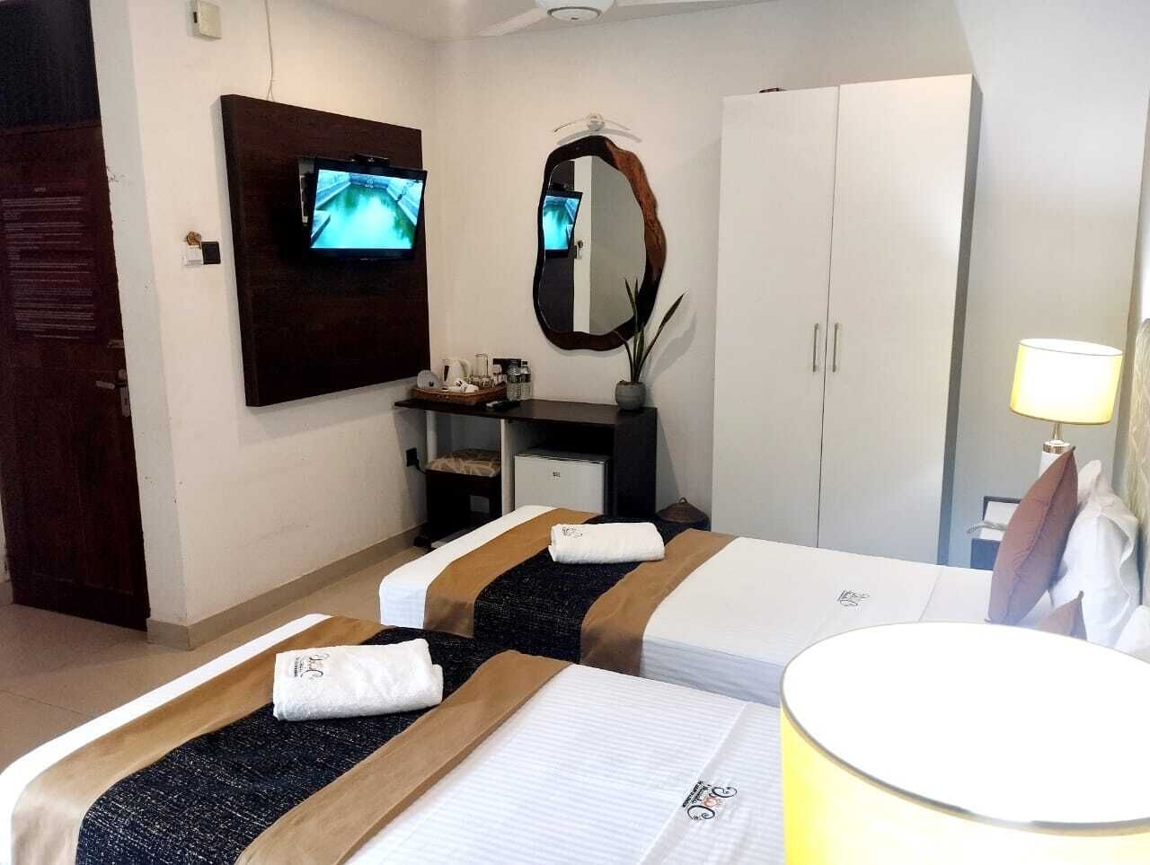 A hotel room with two beds, a TV, a mirror, a wardrobe, and a bedside table with a lamp.