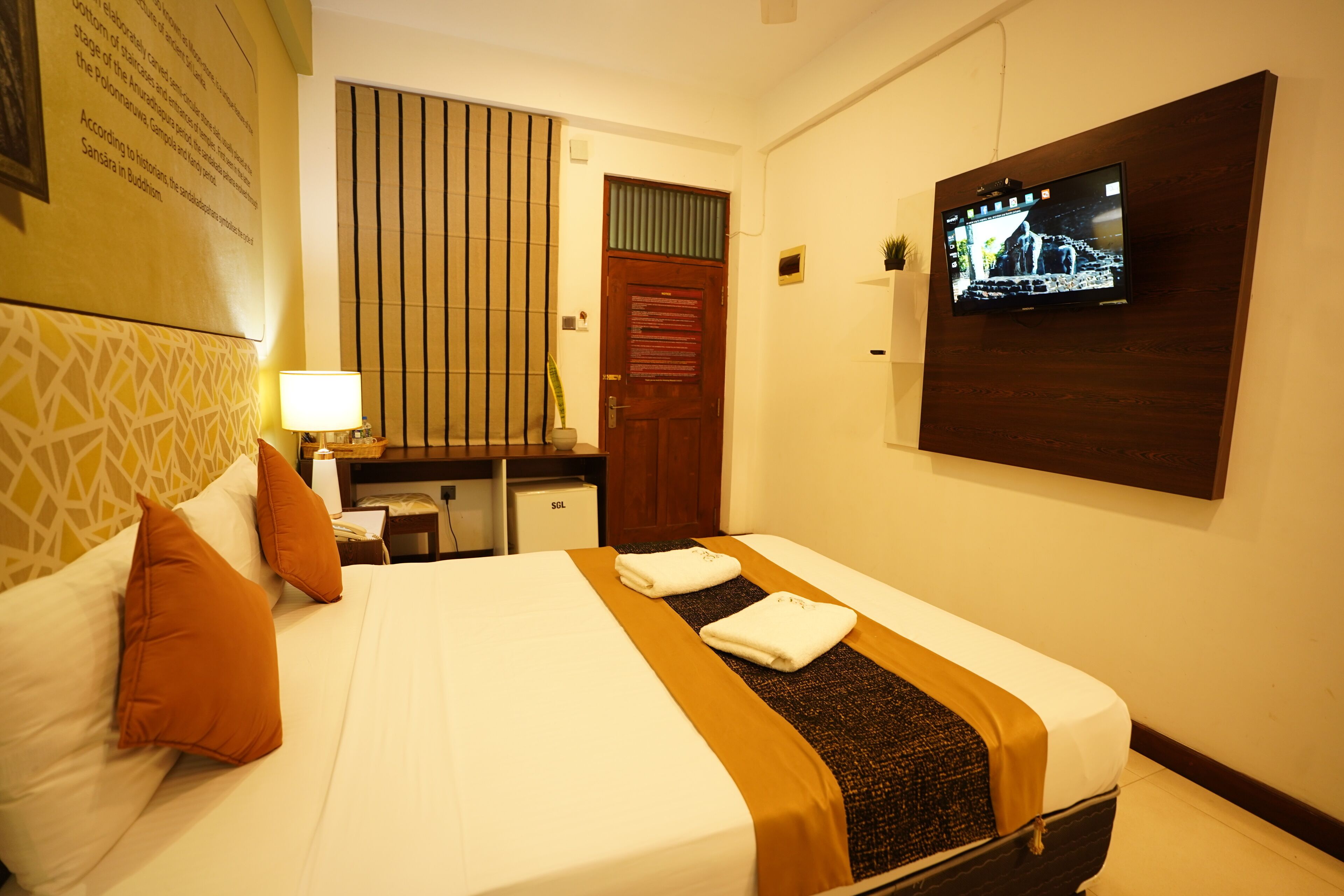 Une chambre d’hôtel avec un lit, un bureau, une télévision et un mur orné d’un tableau encadré.