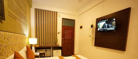 Une chambre d’hôtel avec un lit, un bureau, une télévision et un mur orné d’un tableau encadré.