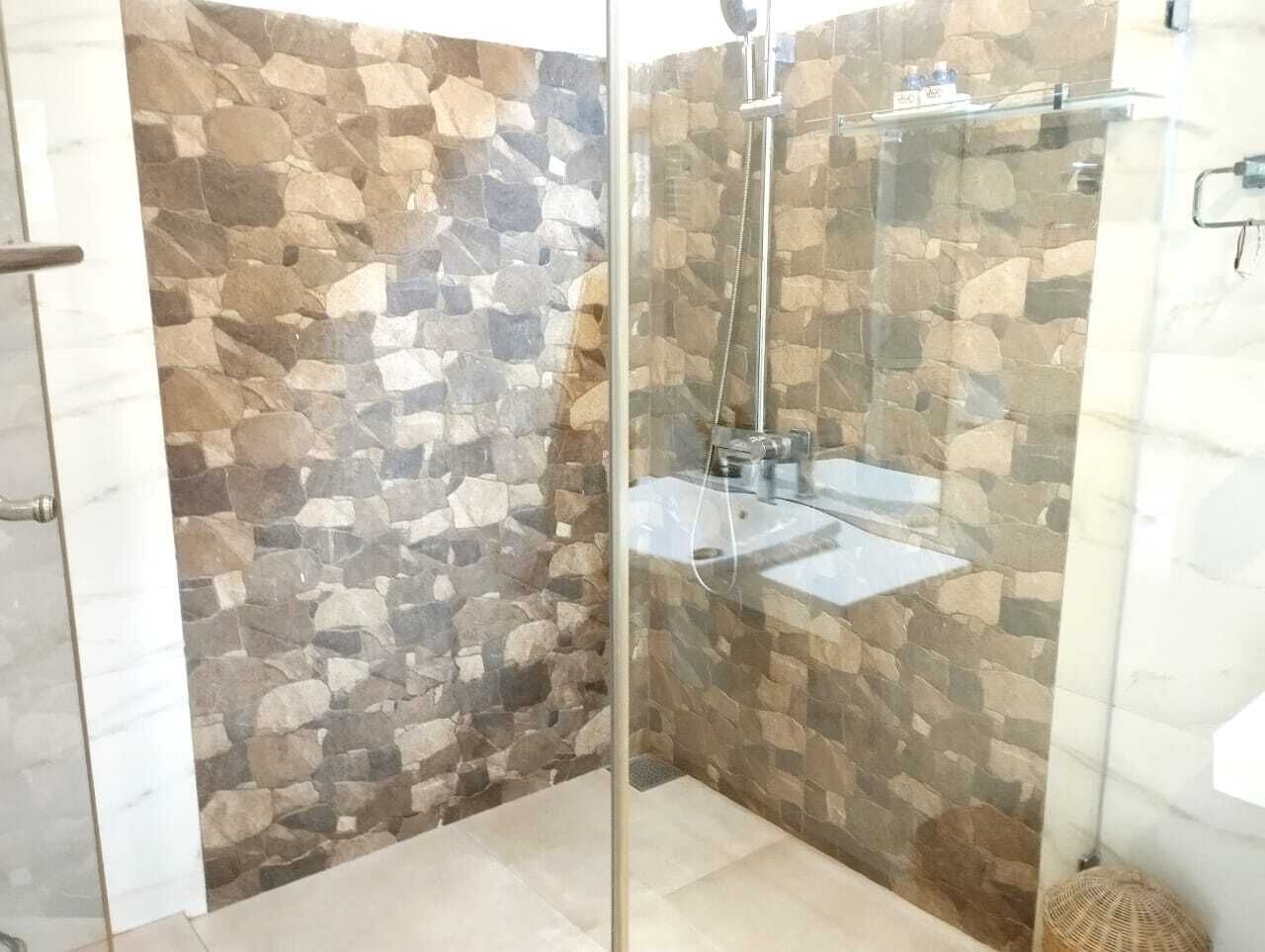 A shower area with a glass door, stone wall, and a handheld showerhead.