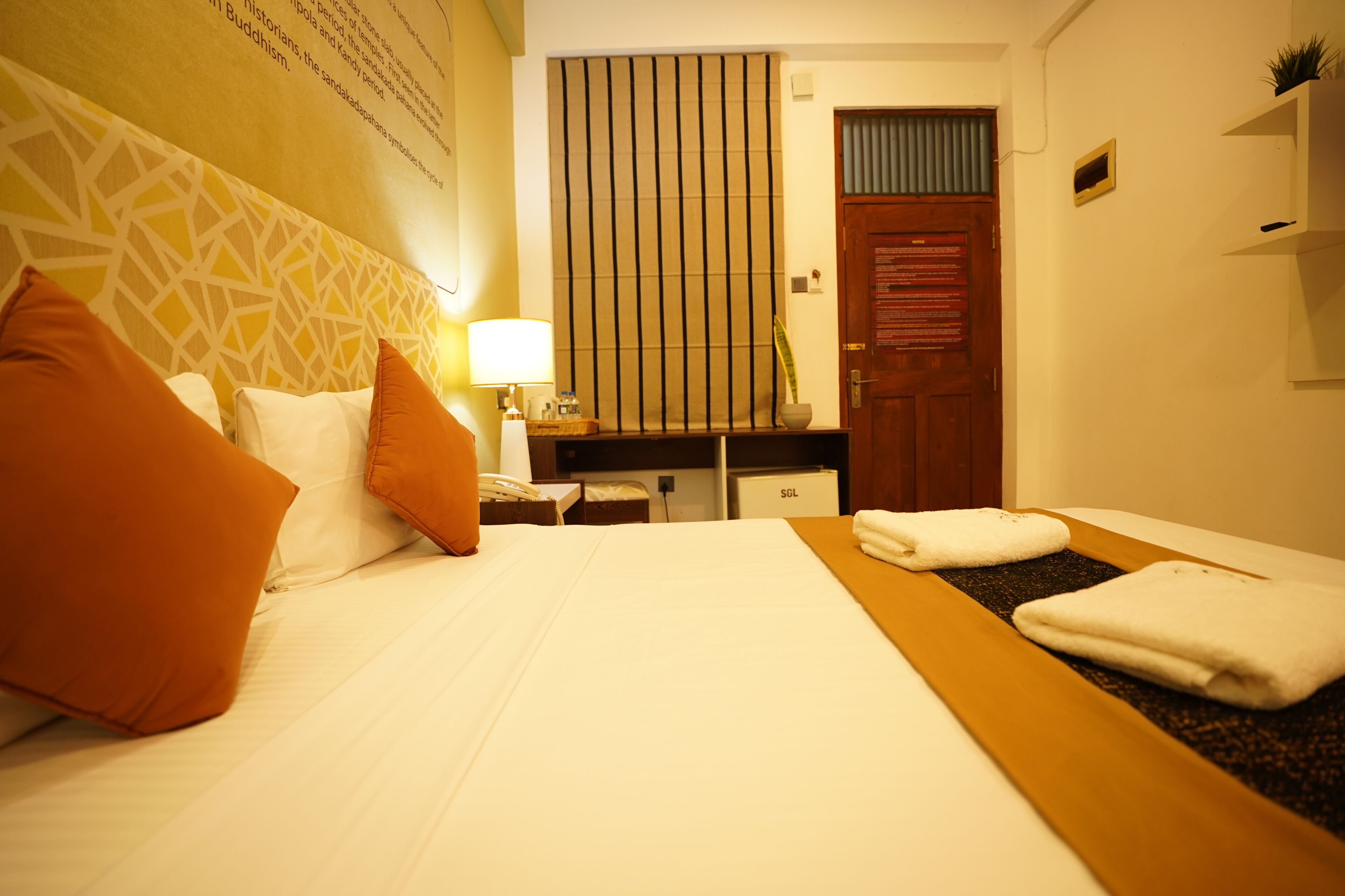 Ein Hotelzimmer mit einem ordentlich bezogenen Bett, einem Schreibtisch mit Lampe und einer Tür.