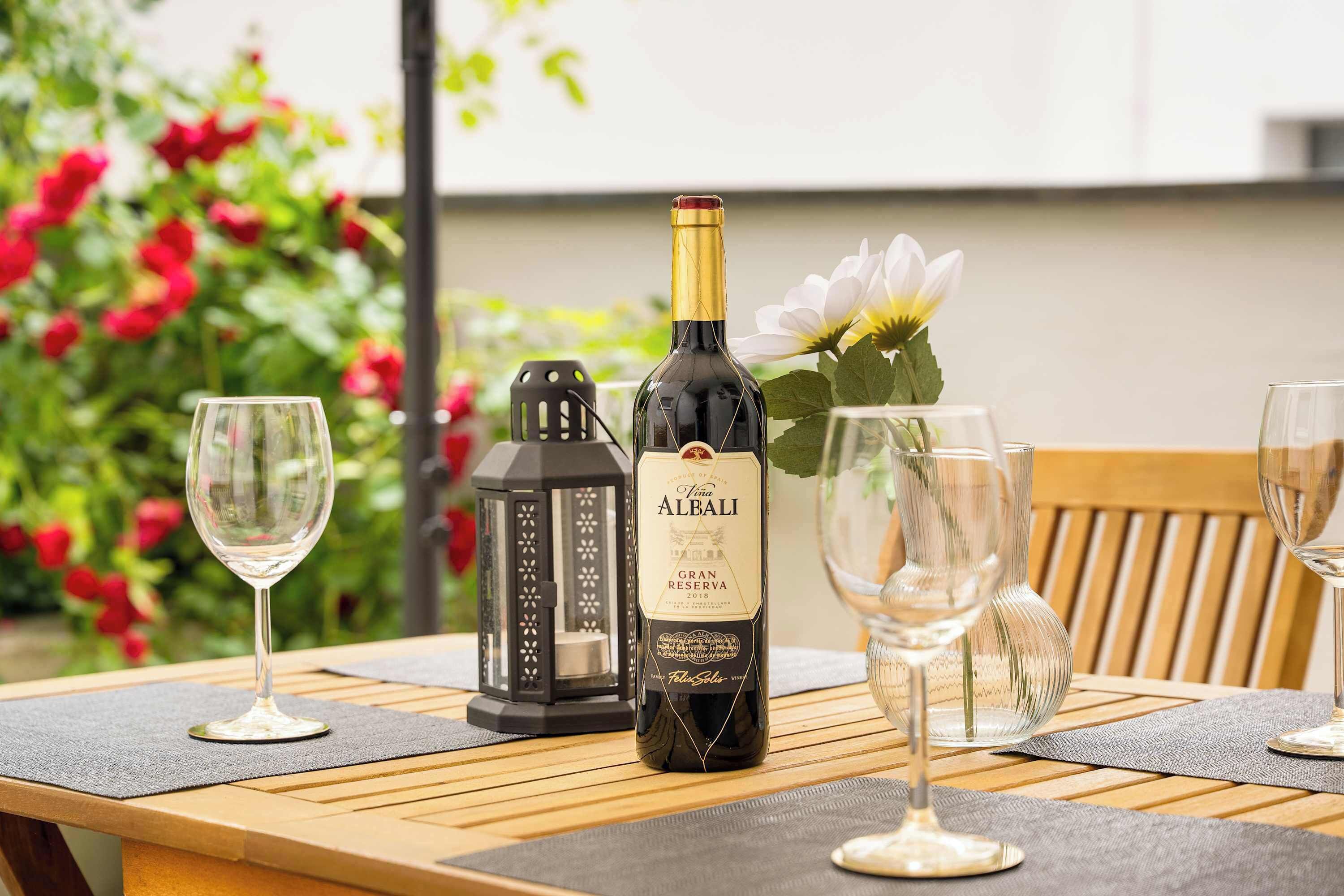 A bottle of wine, glasses, and a lantern on a wooden table with a flower.
