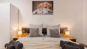 A double bed with a beige blanket, two pillows, a small bedside table with a lamp, and a wall-mounted picture of flowers. - MOLA Apartments-Altstadtwohnung mit Terrasse (Iserlohn)