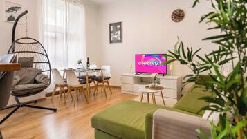 A modern living room with a hanging chair, a dining area, a flat-screen TV, and a green sofa.