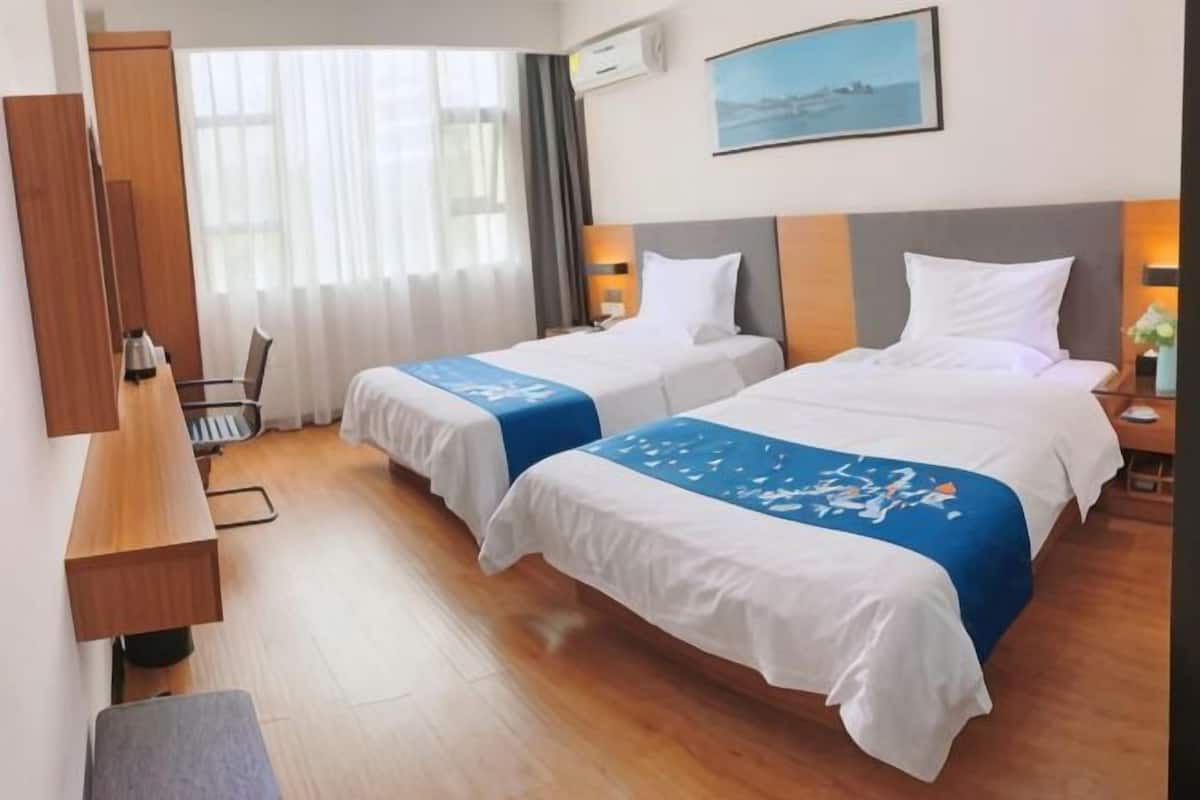 A hotel room with two beds, a desk, a chair, and a window with curtains.