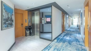 A hotel corridor with a blue patterned carpet, wooden doors, and a framed cityscape painting on the wall. - Yeste Hotel (Yulin Culture Square) (Yulin)
