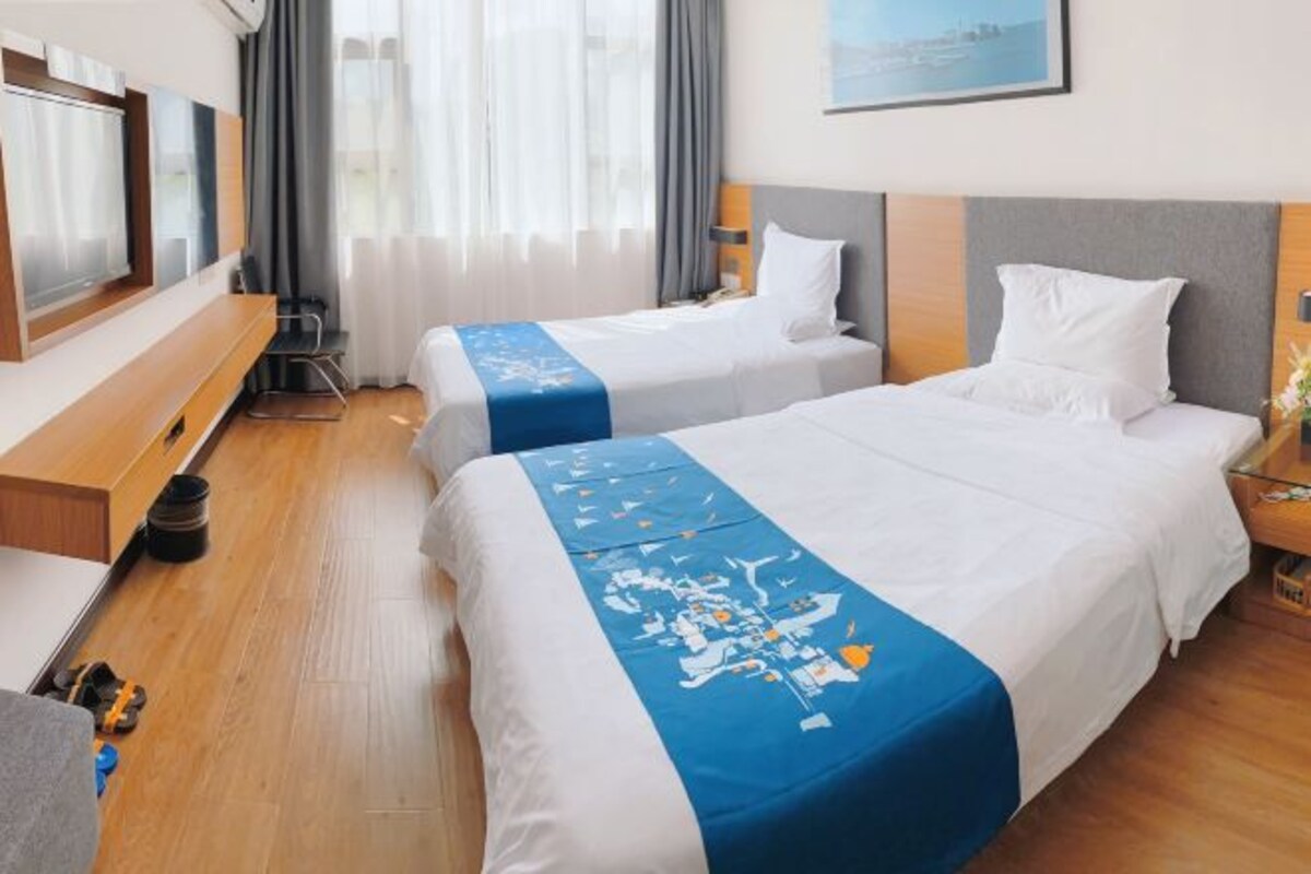 A hotel room with two beds, a TV, a desk, and a window with curtains.