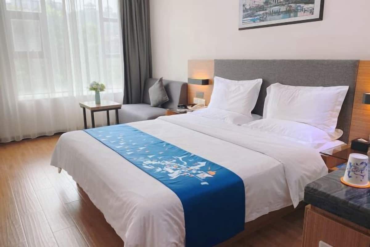 A hotel room with a bed, bedside tables, a nightstand, a small table with a vase, and a painting on the wall.