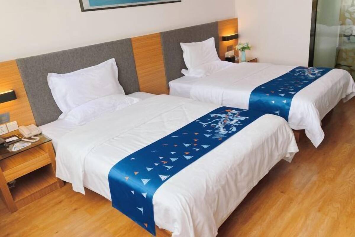 A hotel room with two beds, wooden headboards, bedside tables with lamps, and a blue decorative bedspread.