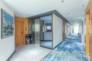 Un pasillo de hotel con piso alfombrado, una recepción y una puerta que da a otra habitación.