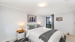 A bedroom with a bed, a nightstand, a window with a view, and two framed pictures on the wall.