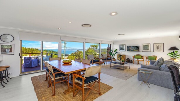 A spacious living area with a large wooden dining table, comfortable seating, and a view of the ocean.