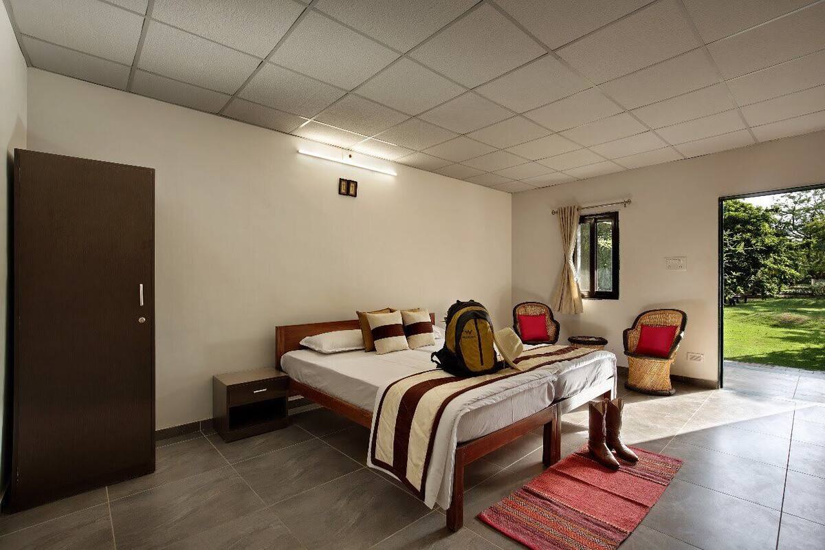 Quarto com cama, guarda-roupa, mesa de cabeceira, cadeira e janela com vista para o verde.