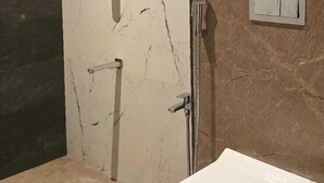 A bathroom with a white bathtub, a shower, and a marble wall. - Vistara Residency (Navi Mumbai)
