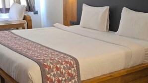 A hotel room with a large bed, a wooden headboard, a bedside table, and a chair. - Vistara Residency (Navi Mumbai)