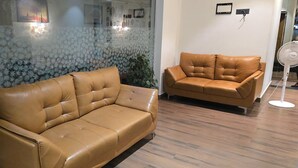 A room with two brown leather sofas and a standing fan. - Vistara Residency (Navi Mumbai)