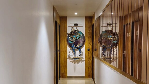 A hallway with a polished marble floor, a wooden door frame, and a decorative wall panel with a circular design. - Vistara Residency (Navi Mumbai)