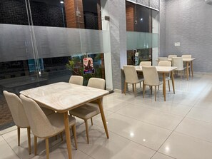 A modern dining area with a glass partition, wooden chairs, and a tiled floor. - Mayoor Hotel  (Udaipurwati)