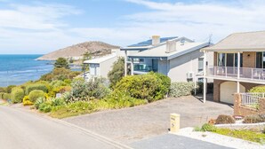 A modern two-story house with a balcony, solar panels, and a view of the sea.