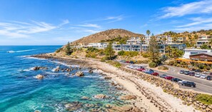 A coastal hotel with multiple buildings, a rocky shoreline, and a clear blue sky.