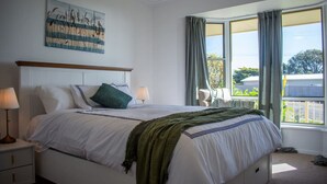A bedroom with a bed, two bedside tables, a nightstand, a window with curtains, and a painting on the wall.