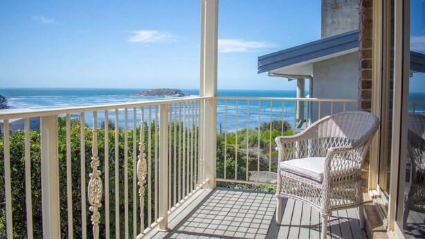 A balcony with a wicker chair, a view of the ocean, and a clear sky.