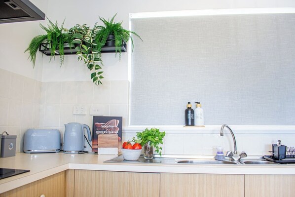A modern kitchen with a built-in sink, a kettle, a toaster, and a potted plant.
