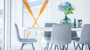 A modern dining area with a white table, grey upholstered chairs, and a vase of flowers.