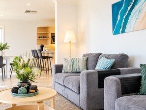 A modern living room with a grey sofa, a round coffee table, and a dining area in the background.