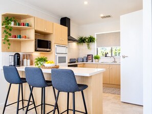 A modern kitchen with wooden cabinets, a central island with bar stools, a microwave, and a stove.