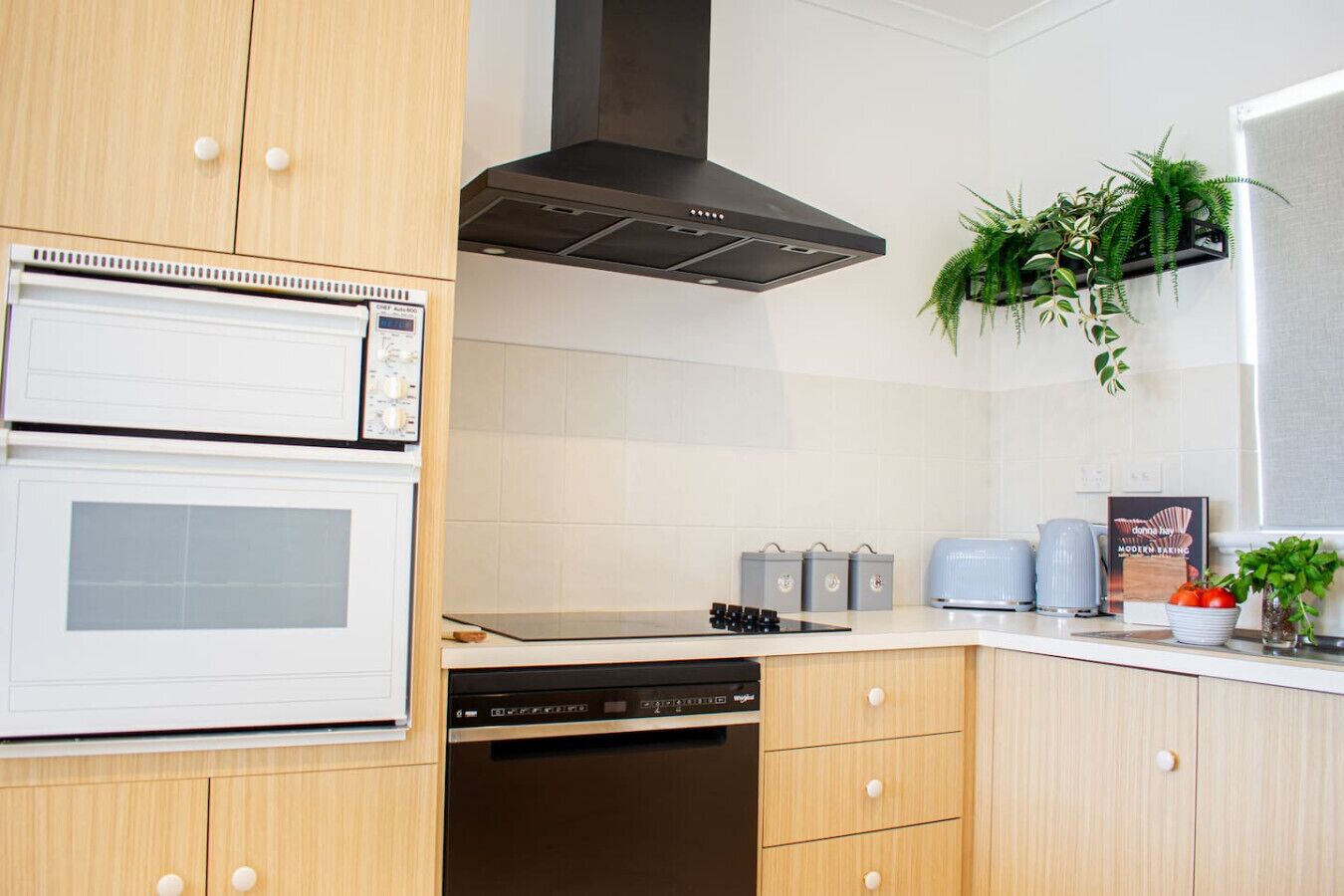 A modern kitchen with a built-in oven, microwave, and dishwasher. There is a gas stove, a range hood, and a plant on the counter.