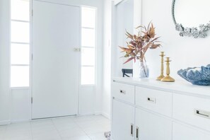 A bright, white room with a large window, a white cabinet with drawers, and a vase with dried plants on the counter.