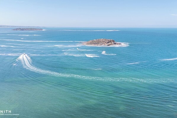 An aerial view of a coastal area with a small rocky island and clear blue waters.