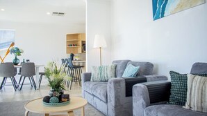 A modern living room with a grey sofa set, a coffee table, and a dining area with chairs and a bookshelf.