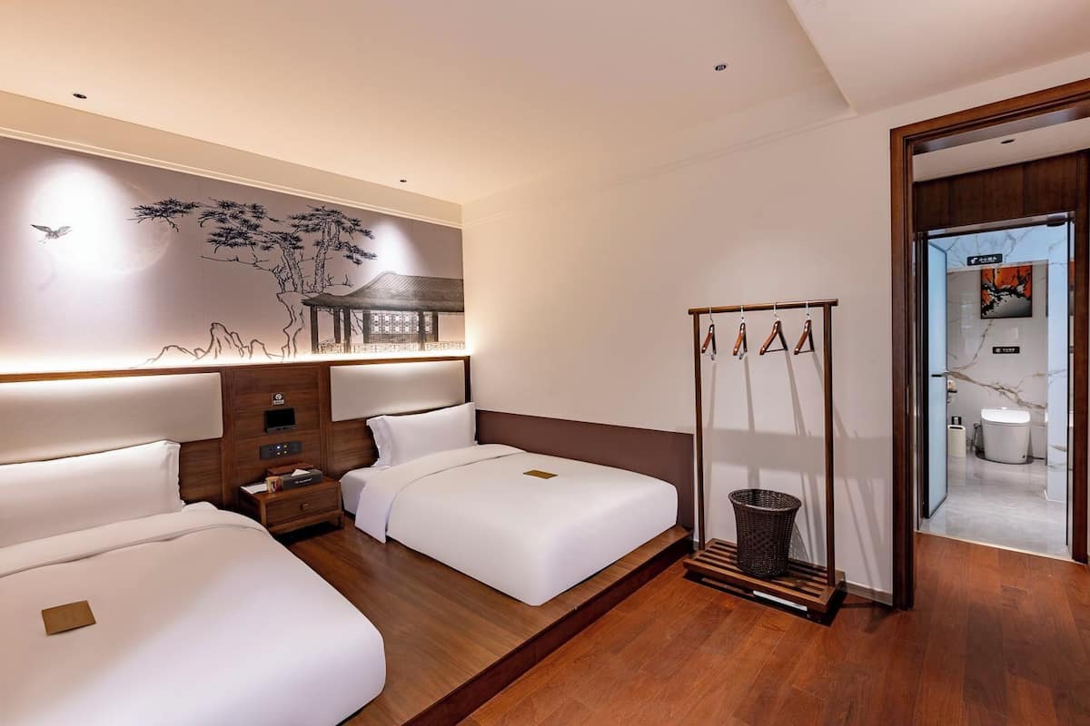 Habitación de hotel con dos camas, cabecero de madera, televisión montada en la pared y armario de madera.