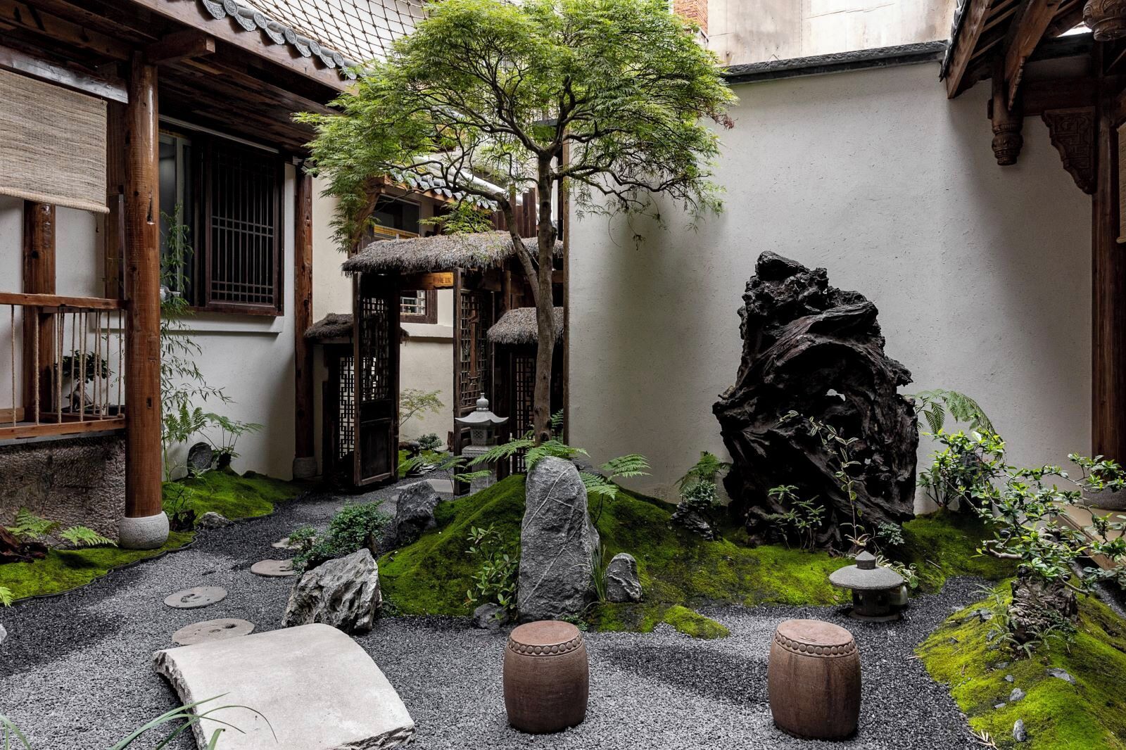 En traditionel japansk have med en stråtækt bygning, moseklædte sten og et stort træ.