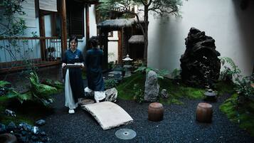 A traditional Japanese garden with a stone pathway, large rocks, and a thatched-roof structure.