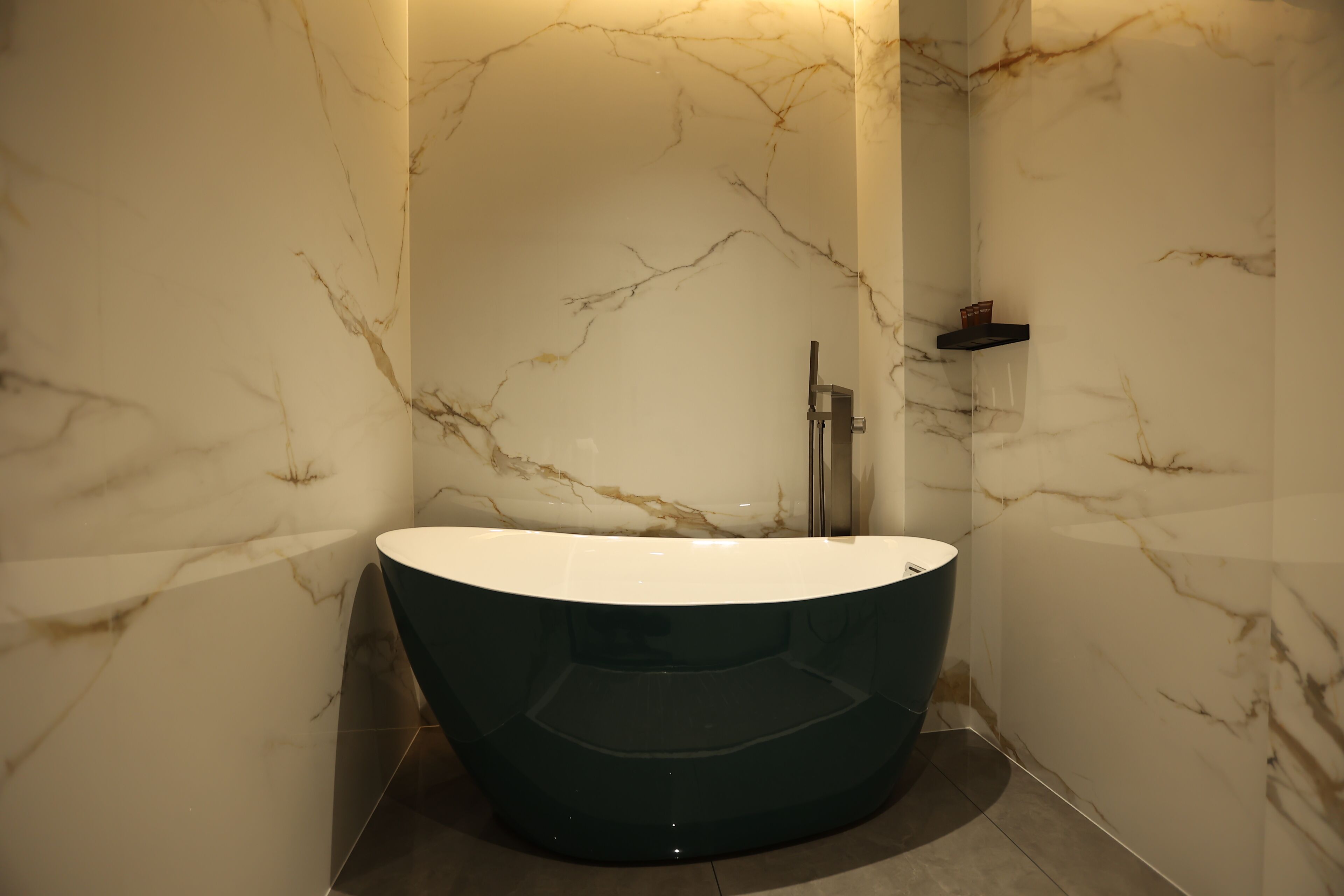 A modern bathroom with a freestanding bathtub, marble walls, and a minimalist shelf.