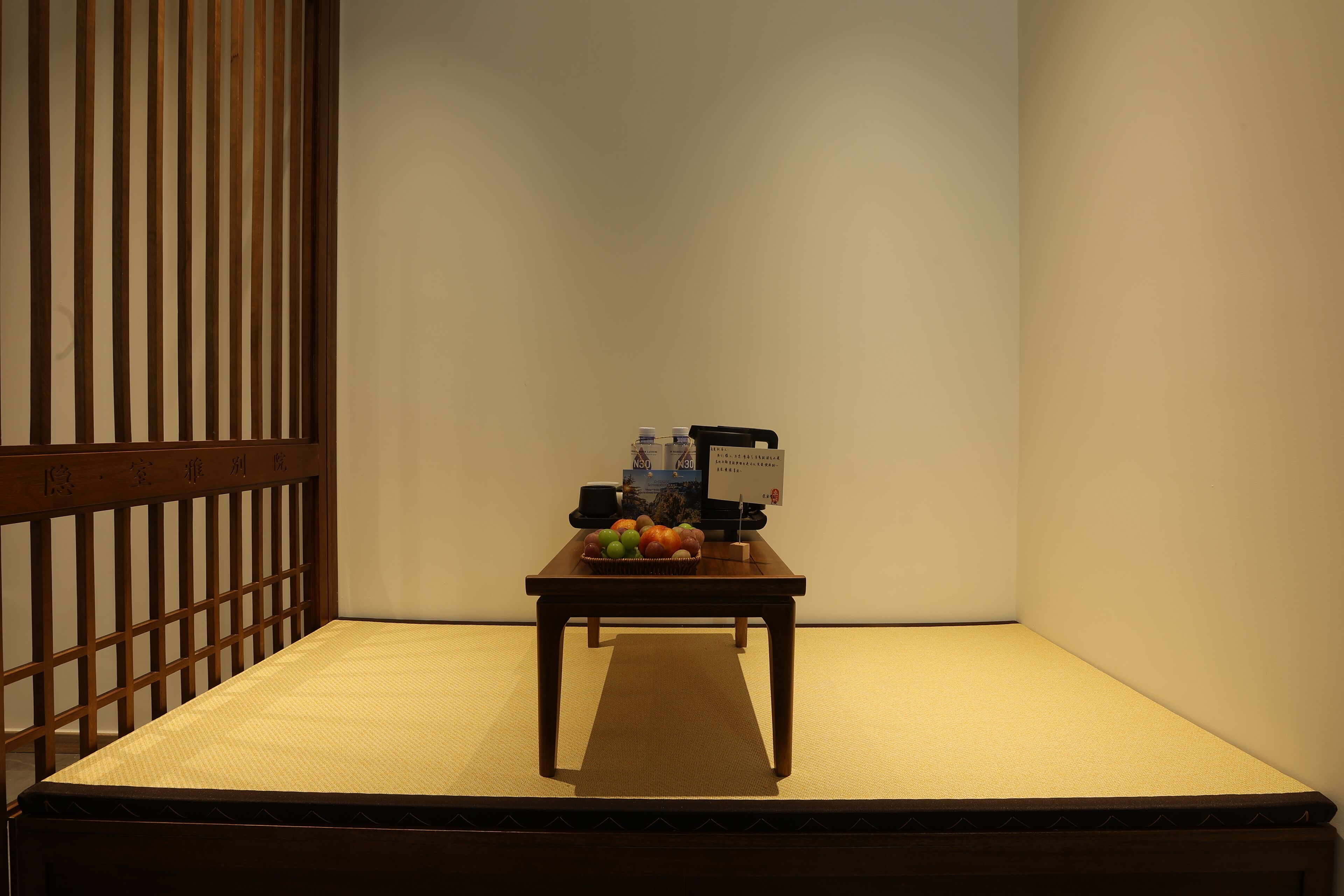 A tatami mat room with a low wooden table, a basket of fruit, and a few bottles.