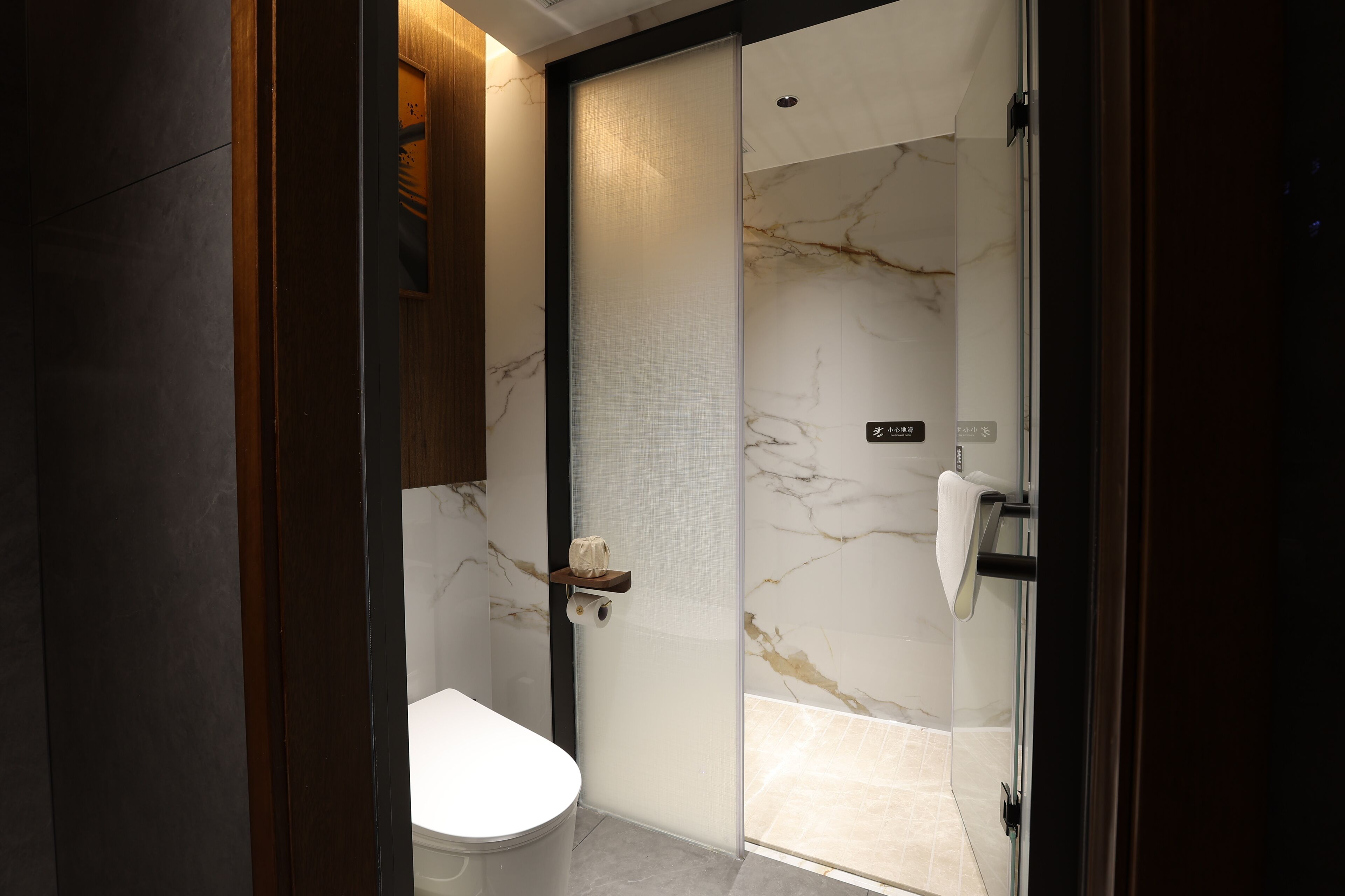 Un baño moderno con inodoro, cabina de ducha de vidrio y pared de mármol.
