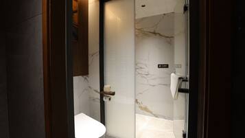 Un baño moderno con inodoro, cabina de ducha de vidrio y pared de mármol.