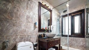 A bathroom with a marble wall, a white toilet, a vanity with a mirror, and a shower area. - AE CRUISE HALONG BAY (Tuan Chau)