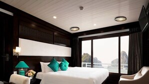 A hotel room with a large bed, a nightstand, a chair, and a view of the water. - AE CRUISE HALONG BAY (Tuan Chau)