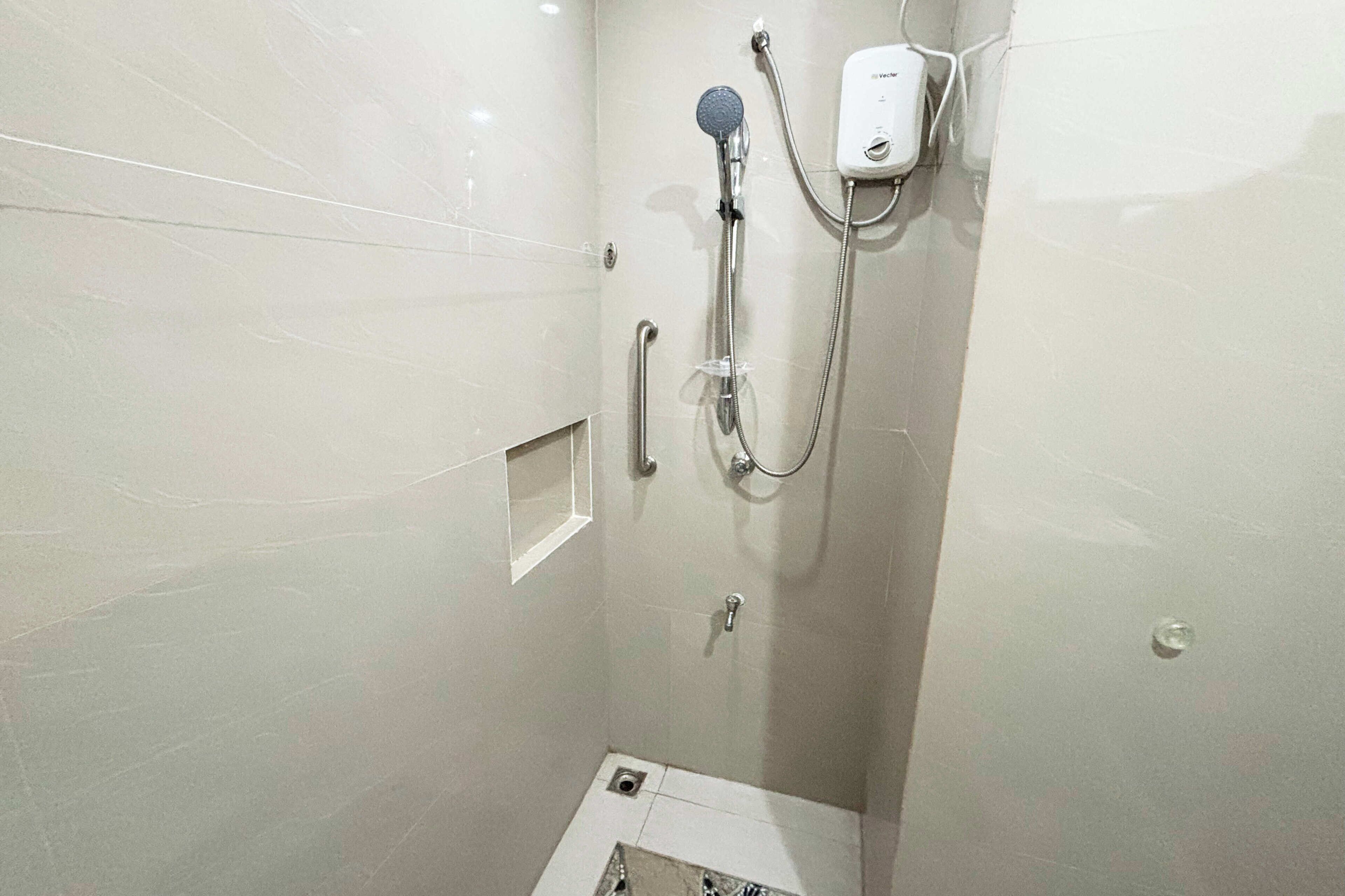A small, modern shower with a handheld showerhead and a wall-mounted control panel.